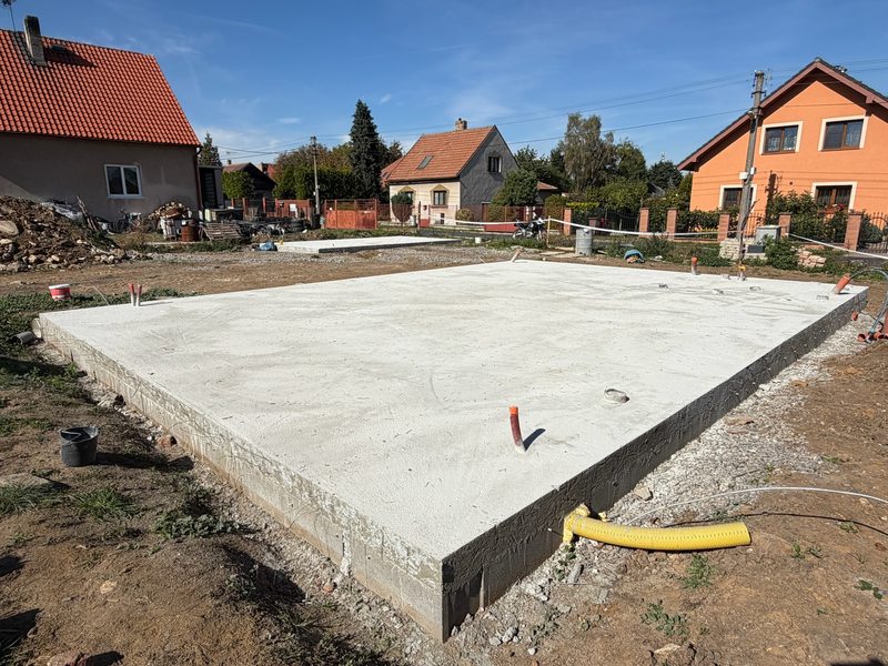 Foto ze stavby: hotová základová deska domu, v pozadí okolní domy